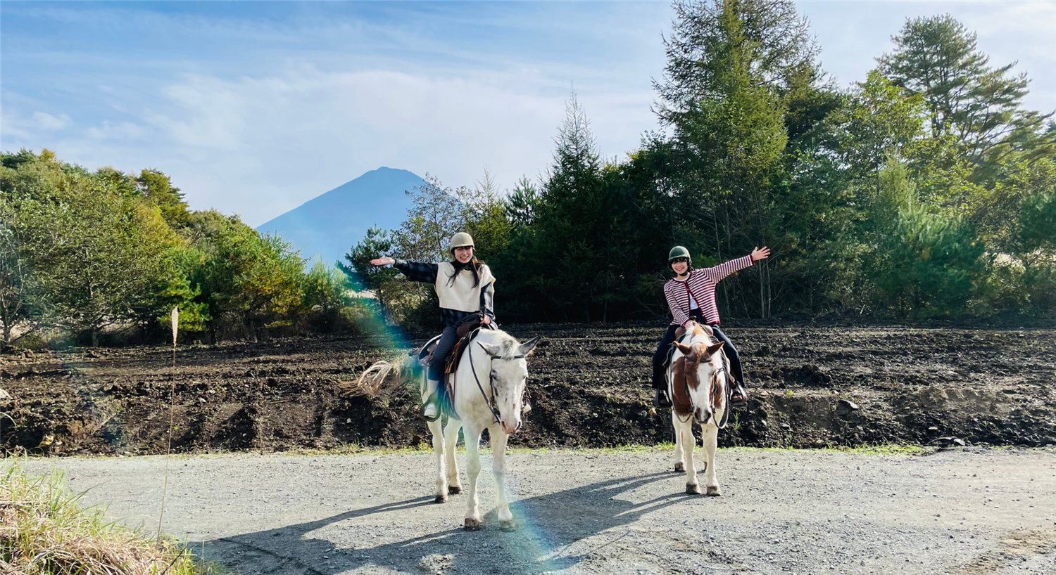 Two riders on horseback spreading their arms with Mt. Fuji in the background